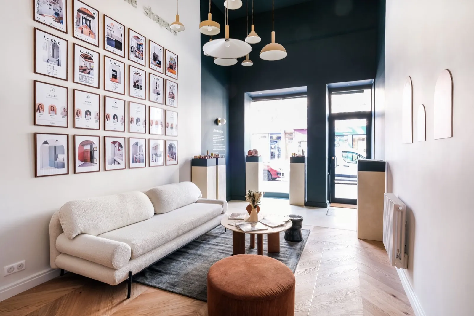 Coin salon côté rue : canapé bouclé, pouf terracotta et mur de projets encadrés — Passage de Lyon
